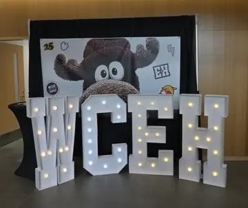 WordCamp Canada sign with large letters WCEH, with a photo backdrop banner featuing a moose.